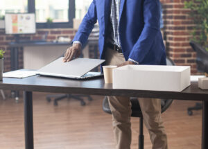 Black man setting laptop on office desk Young male employee with spectacles, carefully arranging his laptop at desk in brick wall workplace. Black businessman setting his digital device on table, preparing for work near office documents.
