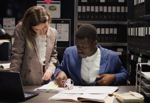 In evidence room, multiethnic private detectives work together to perform criminal investigations. African american and caucasian inspectors use laptop and case files to gather clues and information.